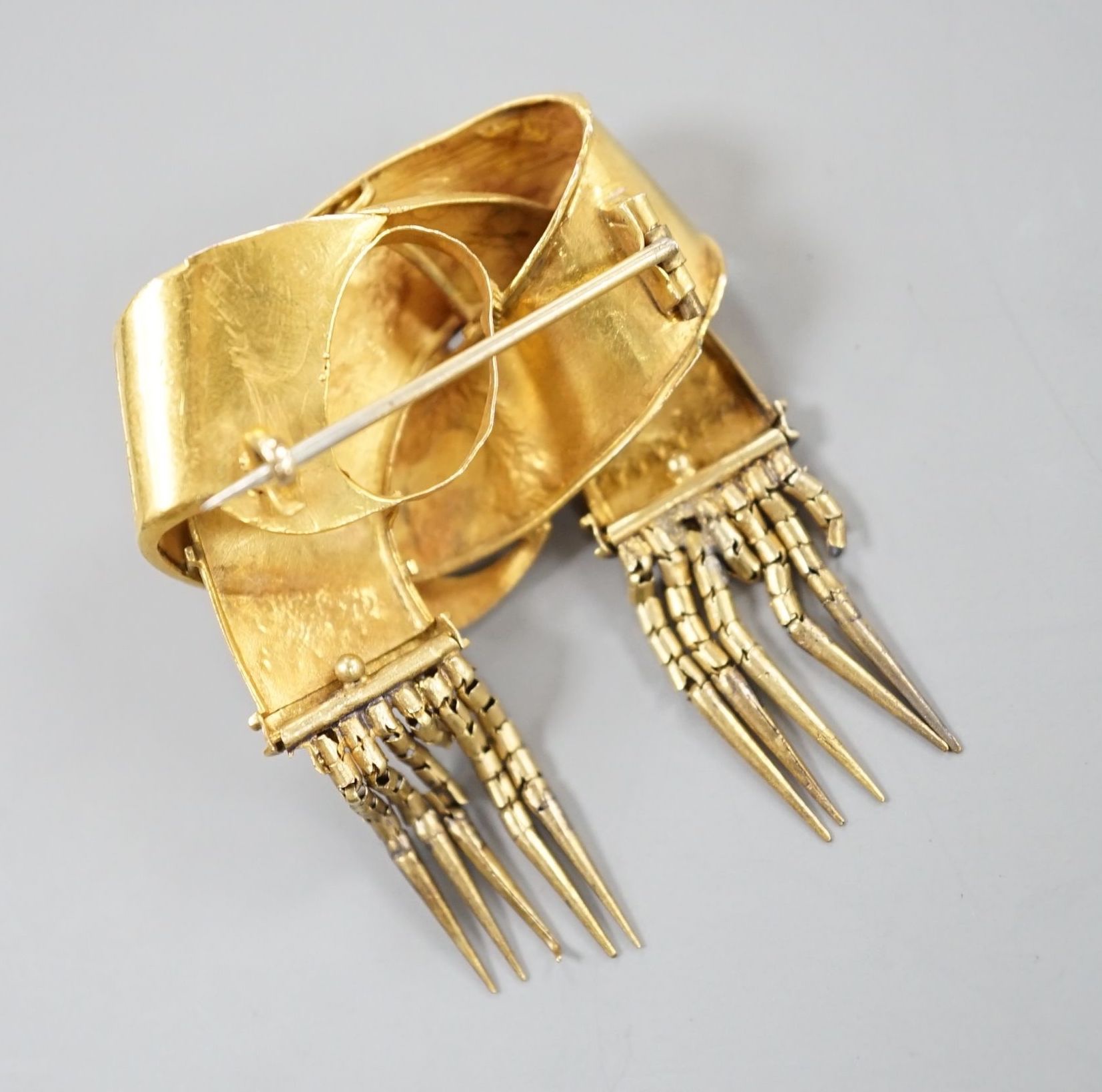 A late Victorian yellow metal entwined buckle and tassel brooch, width 30mm, 6.8 grams.